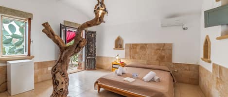 Quarto com uma escultura de árvore em madeira, uma cama com toalhas, uma pequena mesa de cabeceira e uma janela com vista.