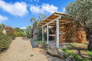 A covered outdoor seating area with a stone wall, a wooden pergola, and a gravel path. - Villa Fontanelle Double Room 1 (Ugento)