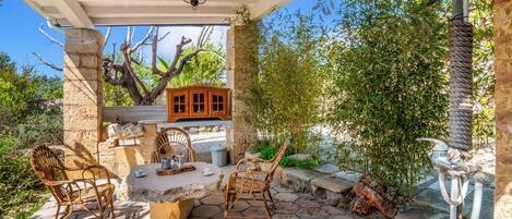 An outdoor patio with hexagonal stone flooring, wicker chairs, a wooden table, and a hanging light fixture.