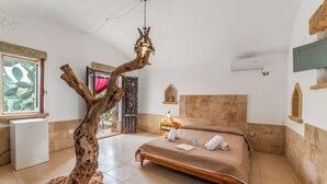 A bedroom with a wooden tree sculpture, a bed with towels, a small bedside table, and a window with a view. - Villa Fontanelle Double Room 1 (Ugento)