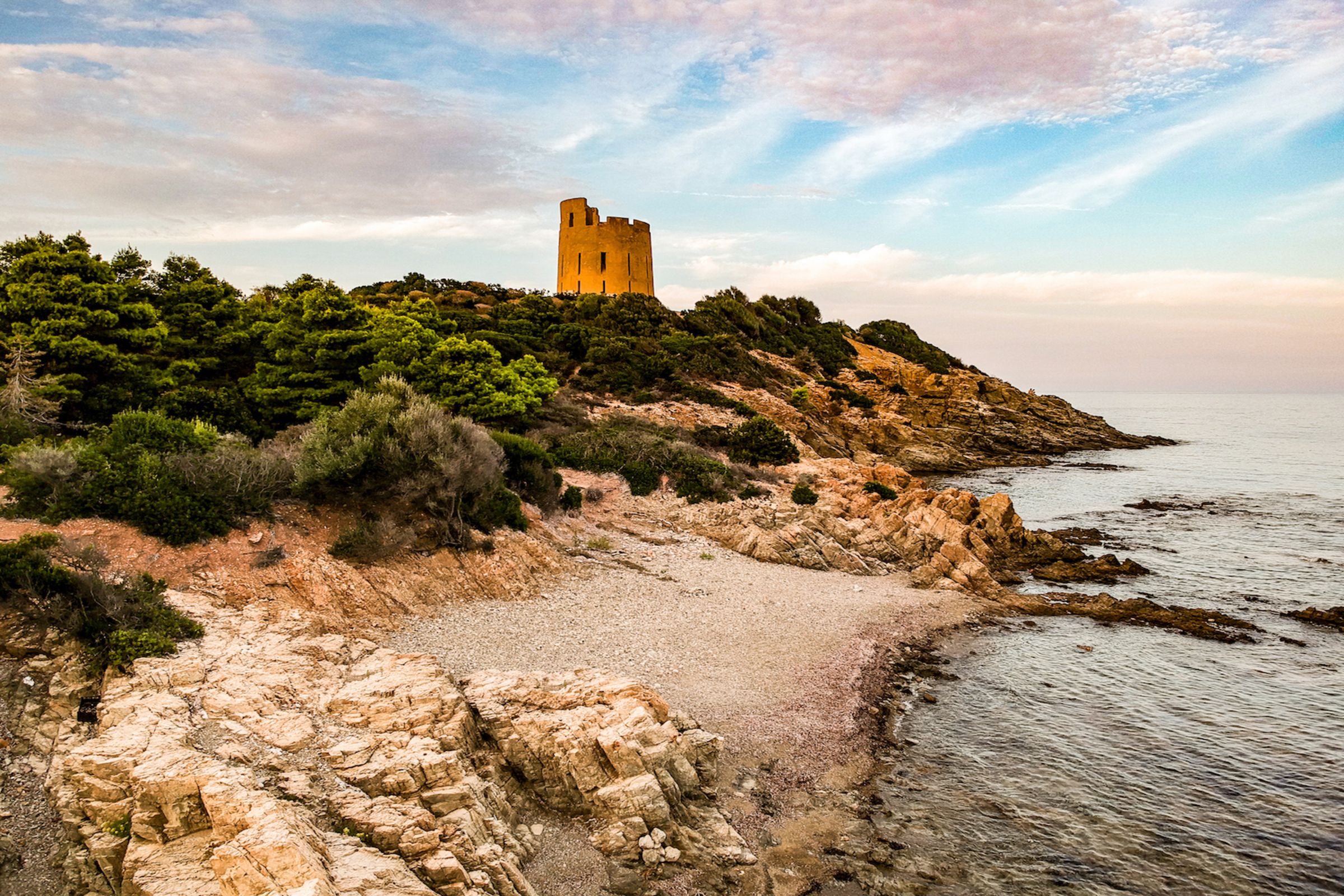 A coastal landscape with a castle on a hill, rocky shoreline, and calm sea.