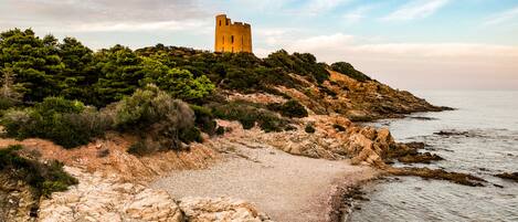 A coastal landscape with a castle on a hill, rocky shoreline, and calm sea.