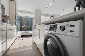 A modern laundry room with a front-loading washing machine, a built-in dryer, and a window providing natural light. - SW DC Waterfront Apt at The Wharf | City Views (Washington)