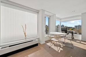 A modern living room with a dining area, large windows, and a view of the cityscape. - SW DC Waterfront Apt at The Wharf | City Views (Washington)