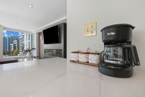 A modern kitchen with a coffee maker, a flat-screen TV, and a view of buildings outside. - SW DC Waterfront Apt at The Wharf | City Views (Washington)