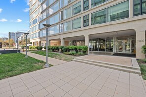 A modern building with a glass facade, a paved entrance area, and a clear sky. - SW DC Waterfront Apt at The Wharf | City Views (Washington)