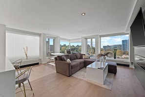 A spacious living room with a large sectional sofa, a dining area with a table and chairs, and a kitchen area with a built-in oven. - SW DC Waterfront Apt at The Wharf | City Views (Washington)