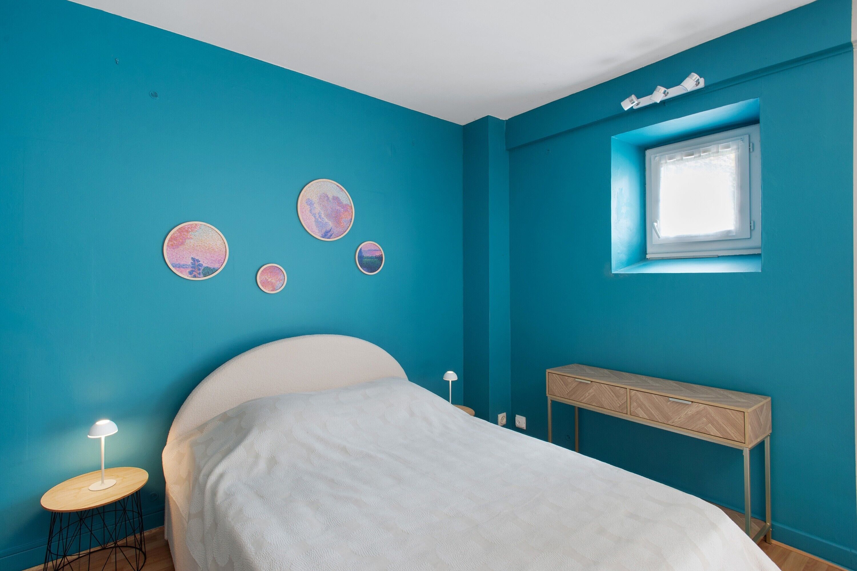 Een slaapkamer met een bed, nachtkastje, raam en wanddecoratie.