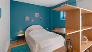 Ein Schlafzimmer mit einem Bett, einem Schreibtisch und einem Sessel. An den Wänden befinden sich Dekorationen und es gibt ein Fenster.