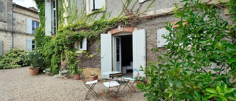 A building with a gravel courtyard, a table with chairs, and potted plants.