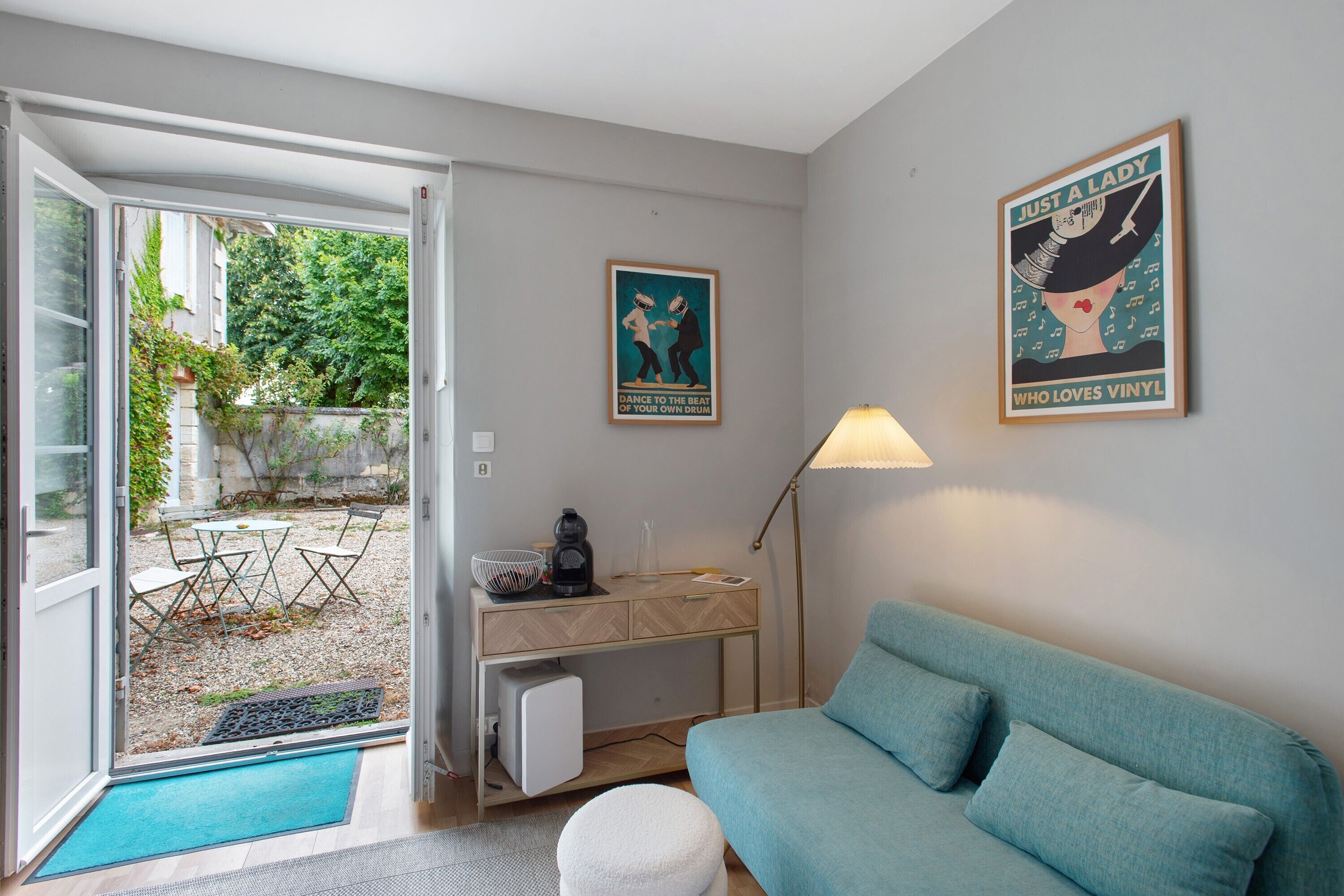 Een kamer met een bank, een bureau met een lamp en twee posters aan de muur.