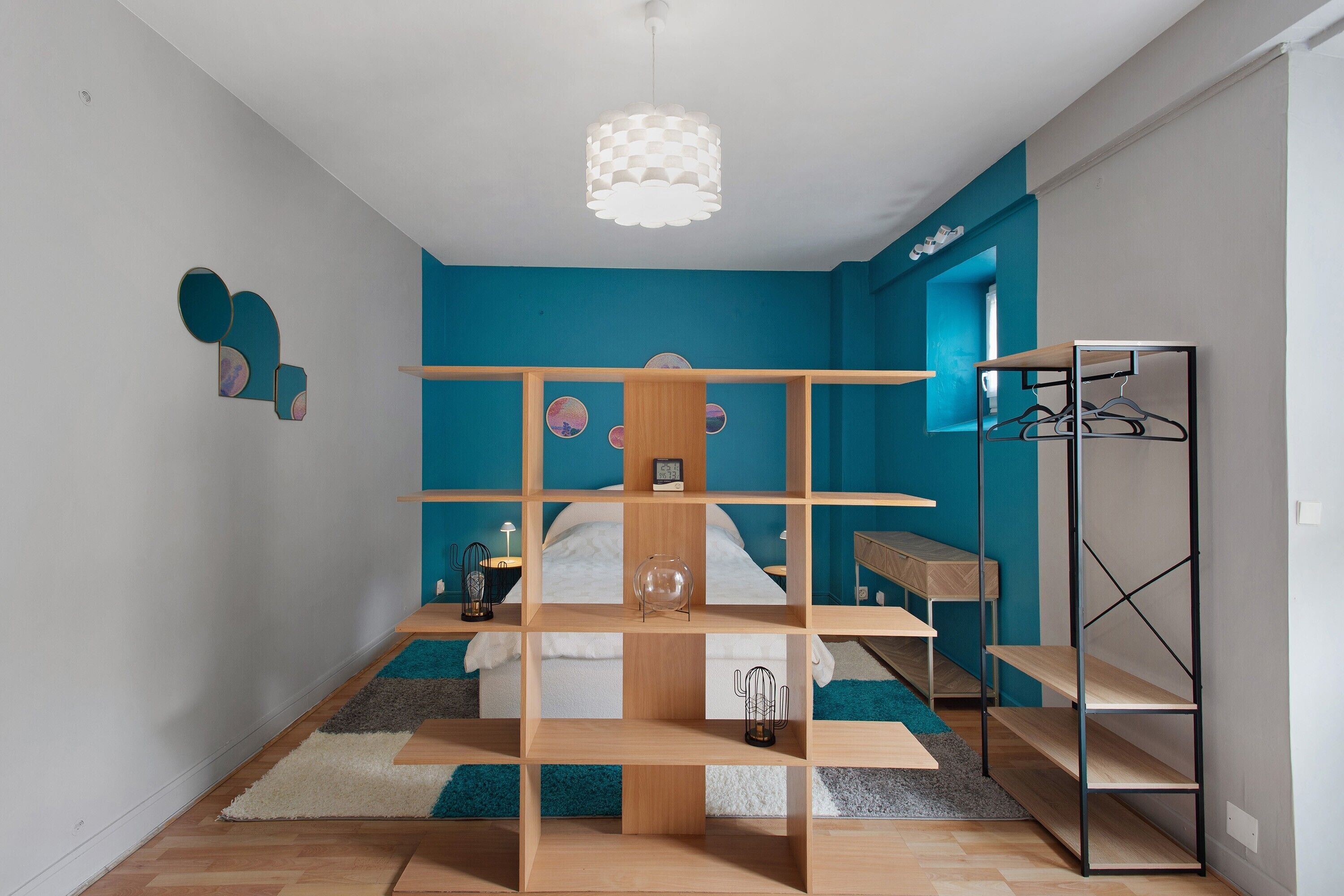 A bedroom with a bunk bed, a desk, a hanging light fixture, and a wardrobe.