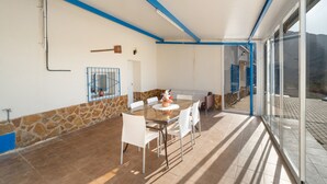 A covered patio with a dining table and chairs, stone wall, and a view through glass doors. - Chalet 'Los Majales' with Private Pool, Wi-Fi, and Air Conditioning (Molina de Segura)