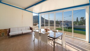 A sunlit room with a glass table and chairs, a sofa, and a view of a pool and mountains. - Chalet 'Los Majales' with Private Pool, Wi-Fi, and Air Conditioning (Molina de Segura)