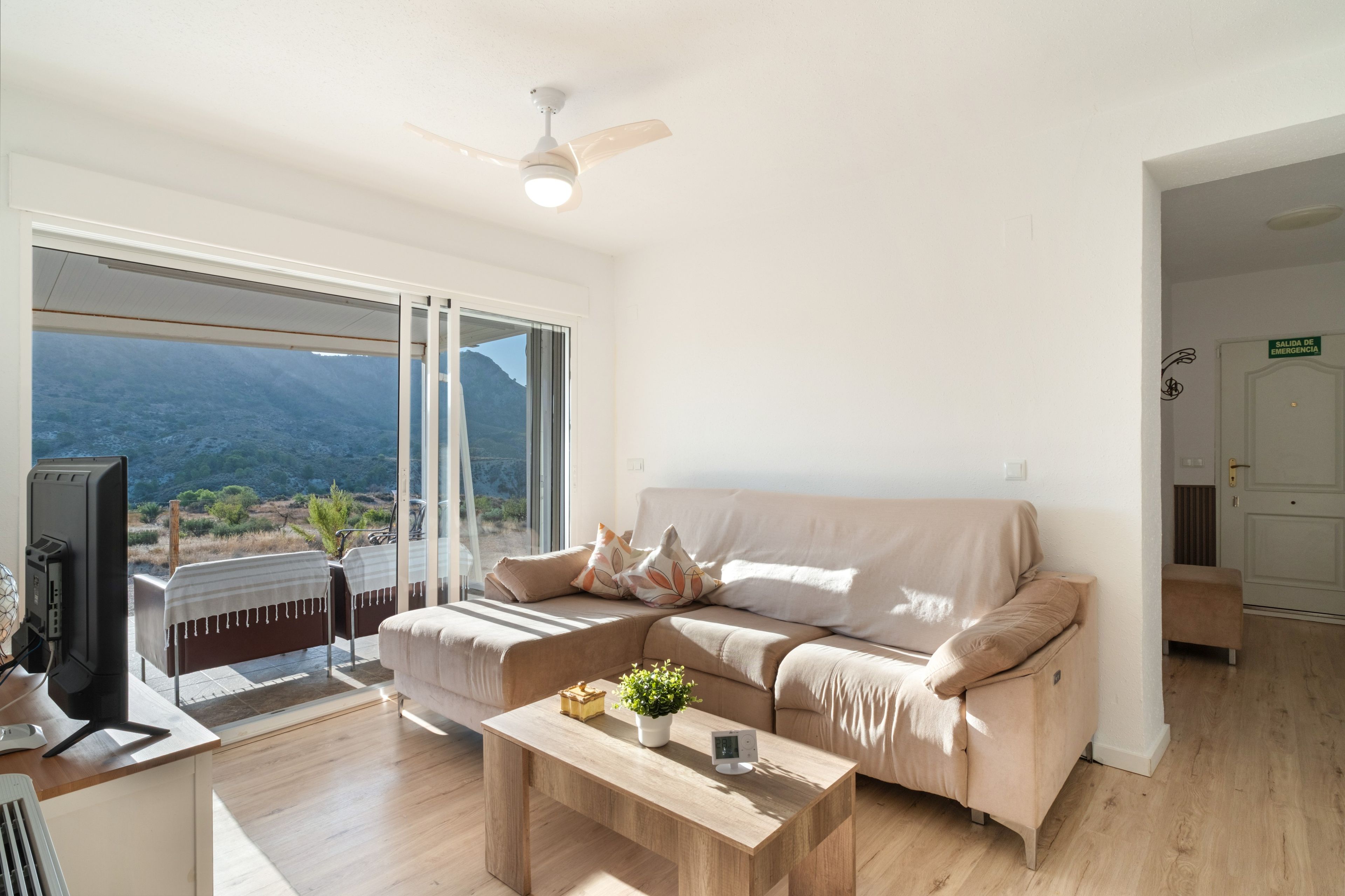Ein modernes Wohnzimmer mit einer Couch, einem Couchtisch, einem Fernseher und Blick ins Freie.