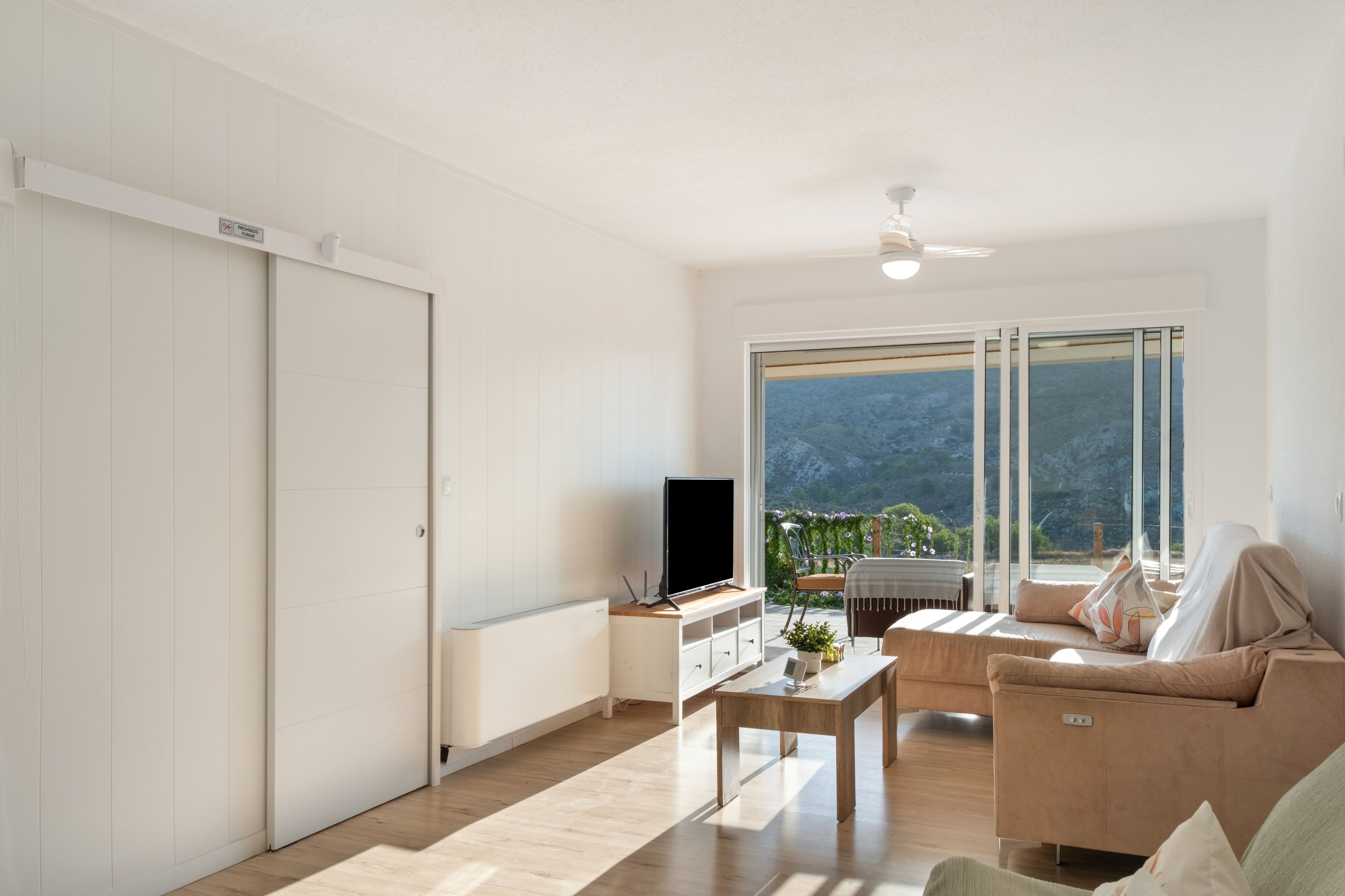 Ein modernes Wohnzimmer mit einem Flachbildfernseher, einem Couchtisch, einer Couch und einer Glastür zum Balkon mit Bergblick.