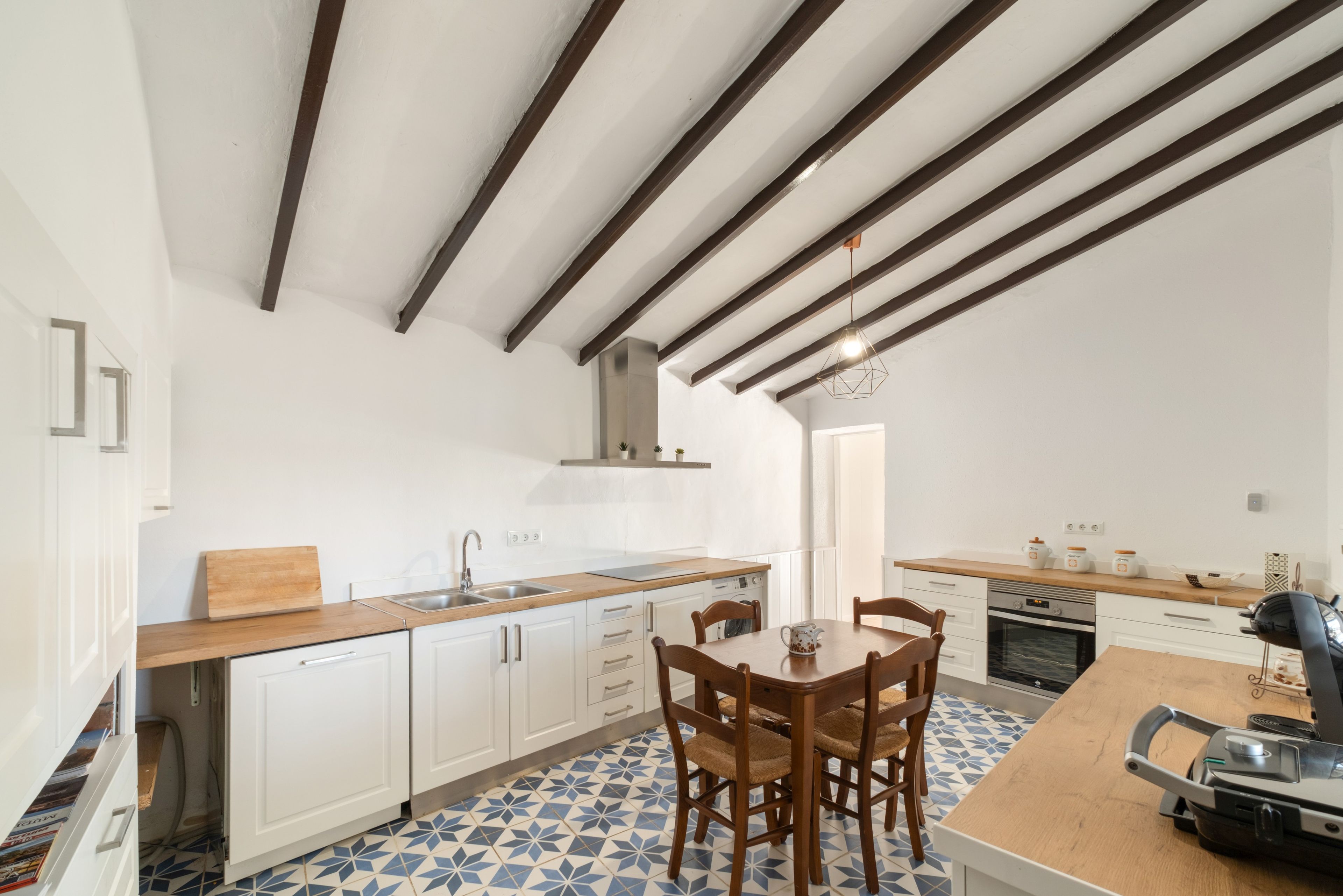 Cozinha moderna com armários brancos, bancada de madeira e área de jantar com mesa e cadeiras.
