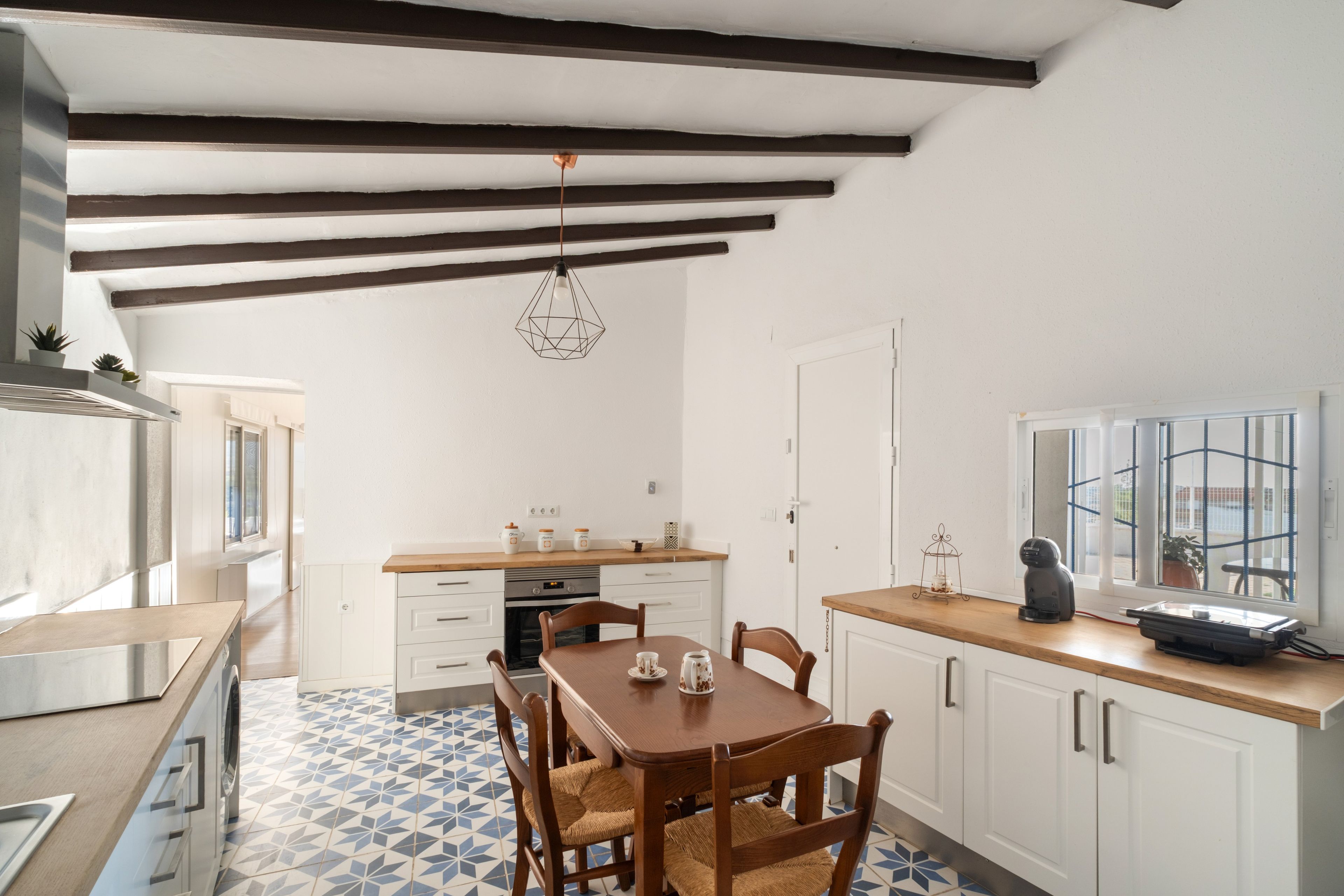 Une cuisine avec des meubles blancs, une table à manger en bois et un luminaire suspendu.