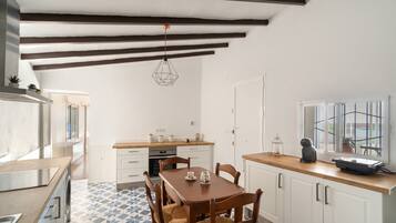 Une cuisine avec des meubles blancs, une table à manger en bois et un luminaire suspendu.