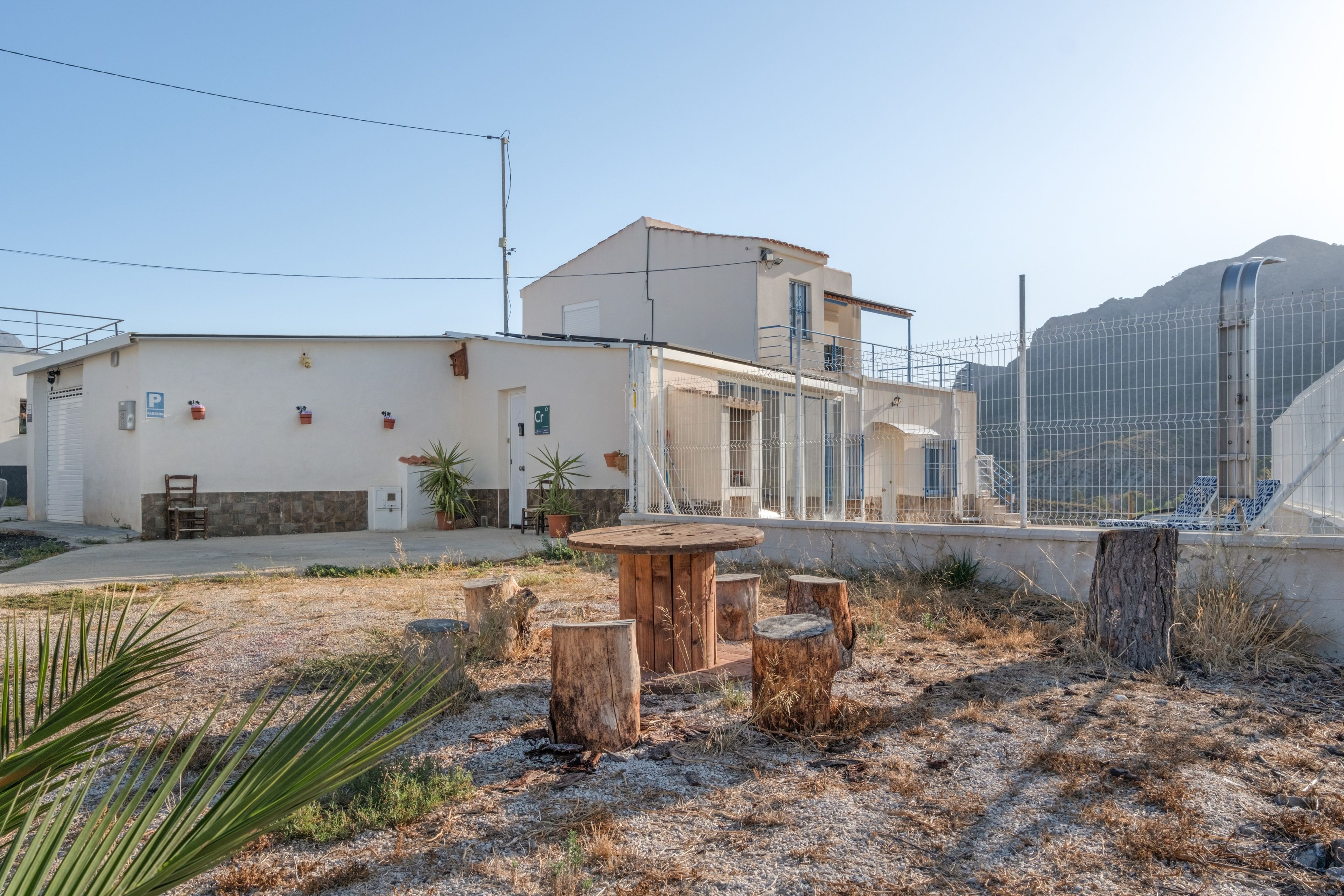 Un edificio residencial con techo plano, balcón y un área cercada con mobiliario exterior.