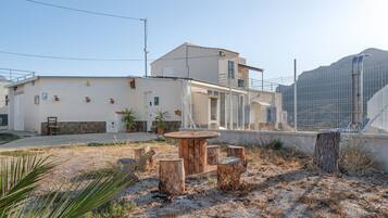 Un edificio residencial con techo plano, balcón y un área cercada con mobiliario exterior.