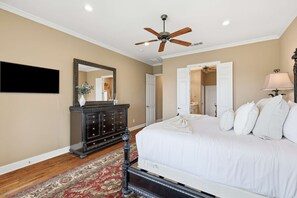 Ein Schlafzimmer mit Bett, Kommode, Spiegel, Deckenventilator und Fernseher.