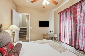 Ein Schlafzimmer mit einem Bett, einem Schreibtisch, einem Stuhl, einem Fernseher und einem Fenster mit Vorhängen.