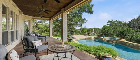 An outdoor patio with a pool, seating area, and ceiling fans.