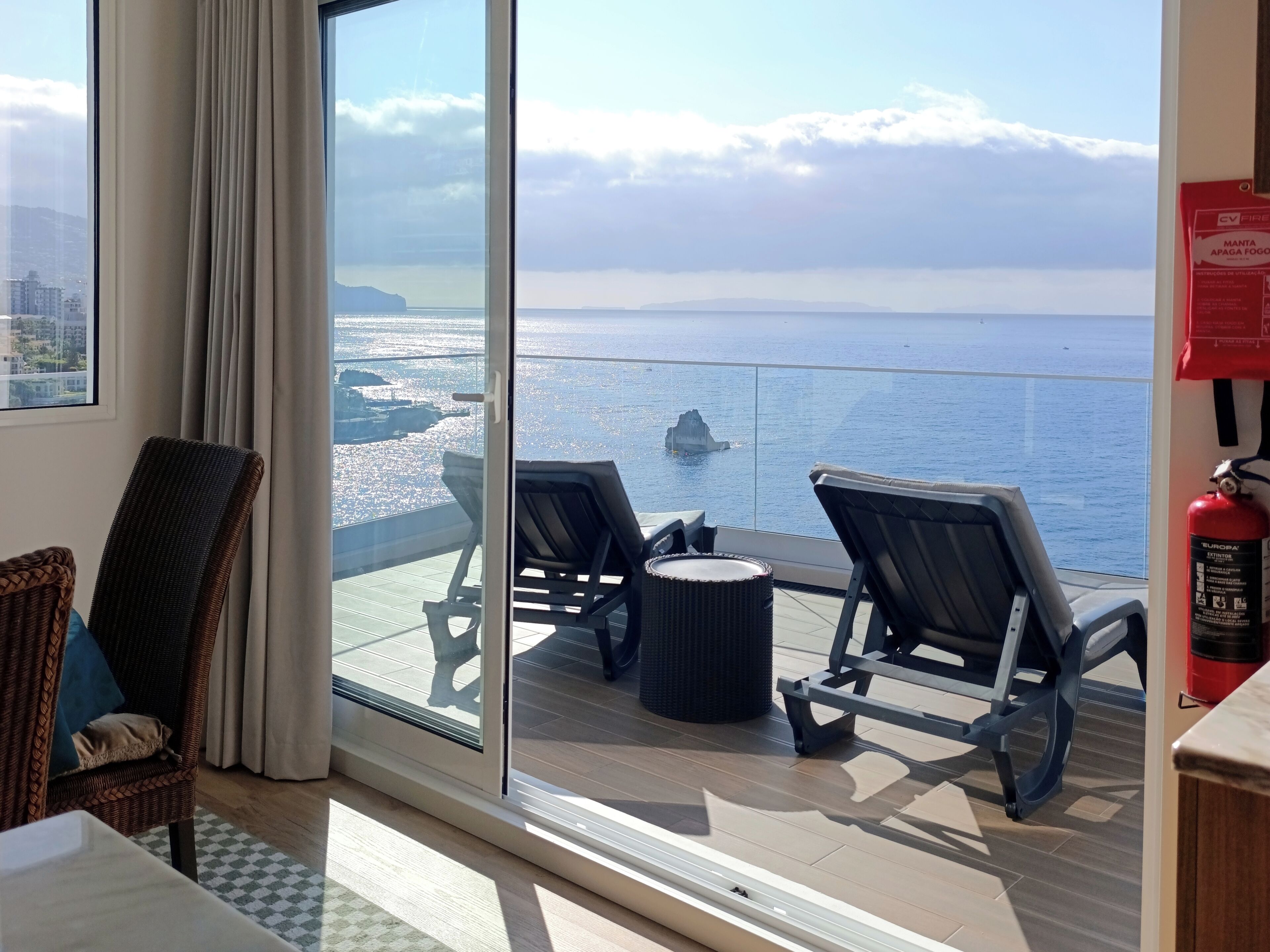 Een balkon met twee loungestoelen, een klein rond tafeltje en uitzicht op zee.