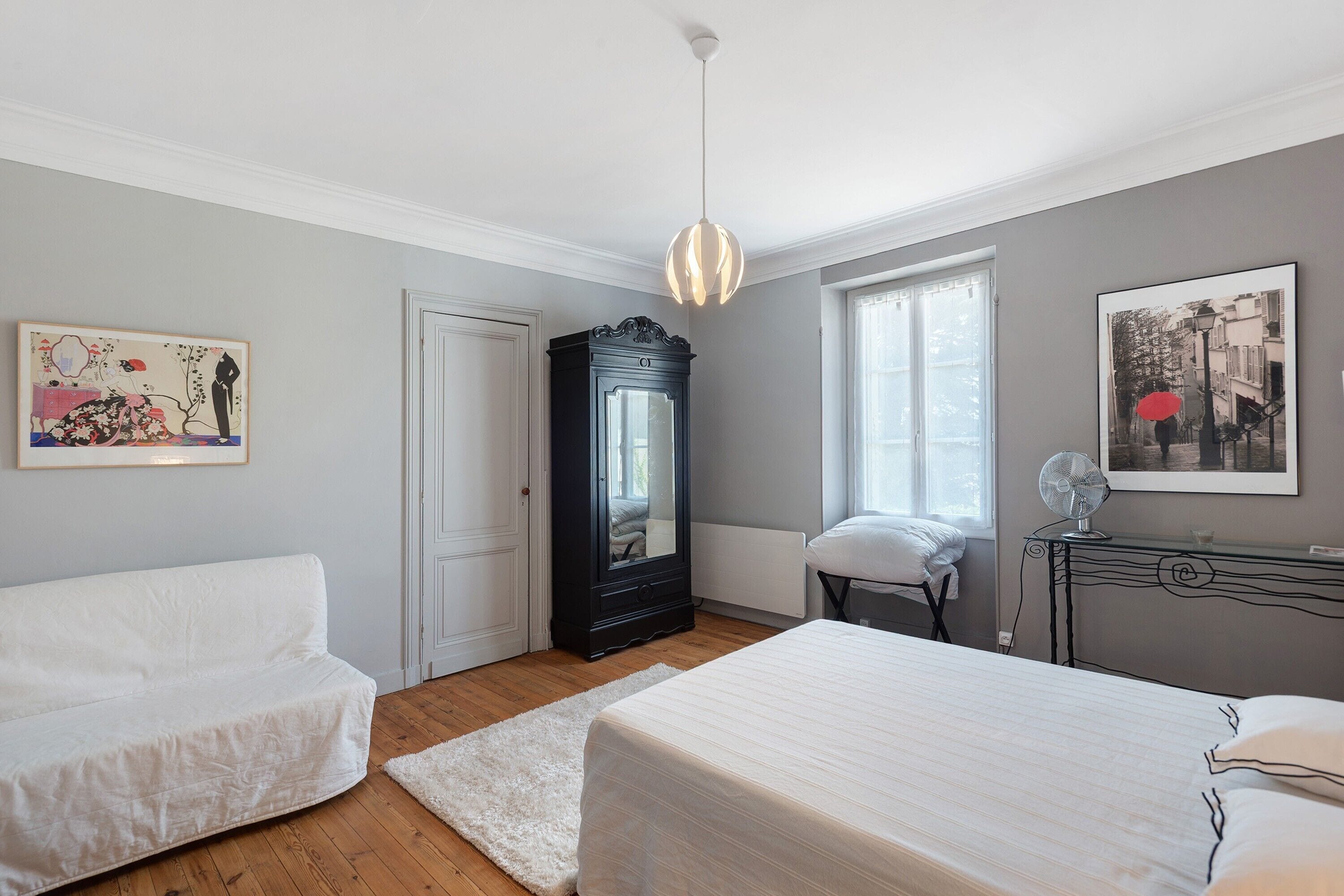 Un dormitorio con cama, una silla, cómoda, espejo y obras de arte en las paredes.