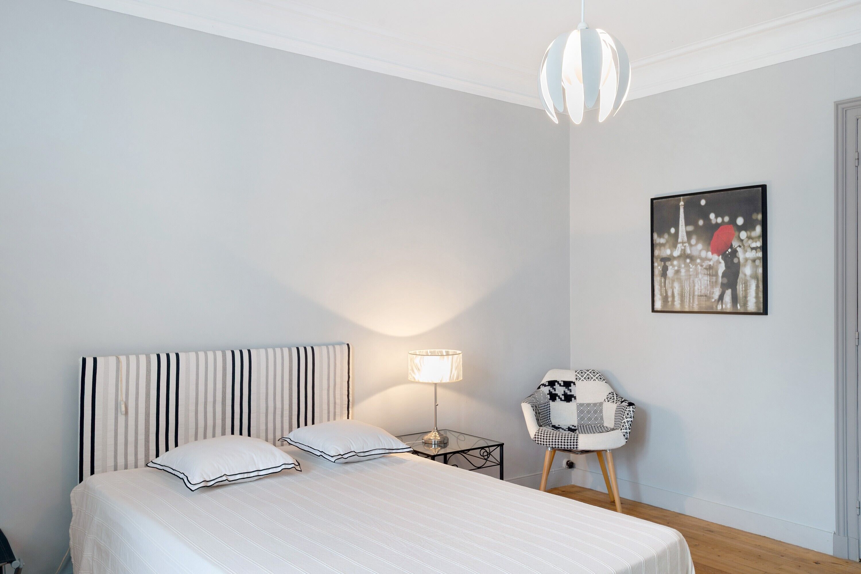 Une chambre à coucher avec un lit, une lampe de chevet, une chaise et un tableau au mur.