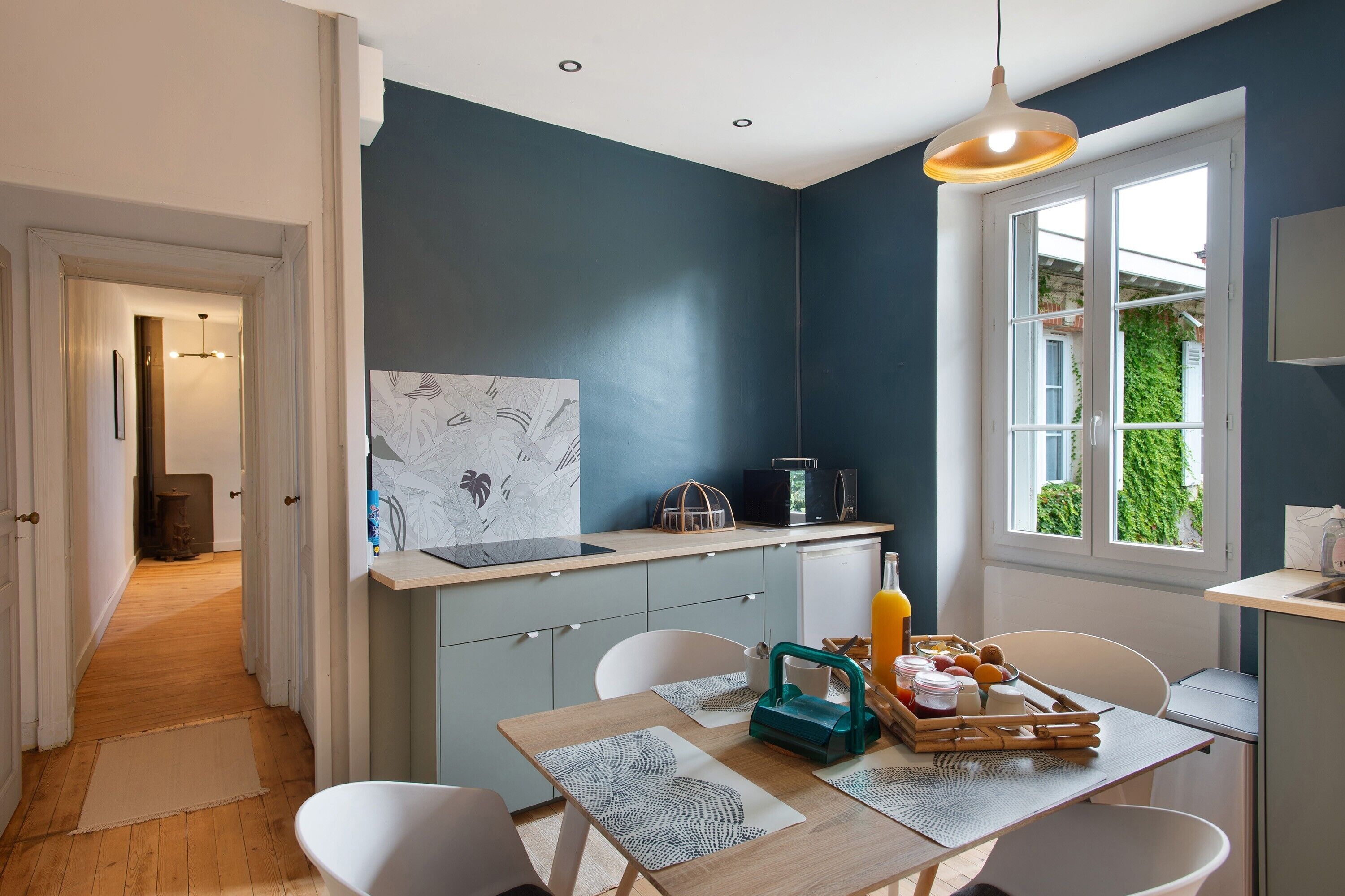 Una cocina moderna con pared azul oscuro, una mesa de comedor de madera con individuales, un microondas y un refrigerador.