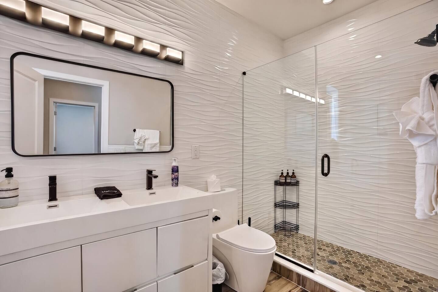 Een moderne badkamer met een douchecabine van glas, een wastafel met spiegel en een toilet.