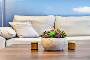 A room with a wooden table, a white sofa with cushions, and a large pot with succulents.