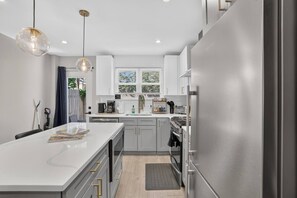Une cuisine moderne avec des meubles blancs, un îlot central, des appareils en acier inoxydable et des luminaires suspendus.