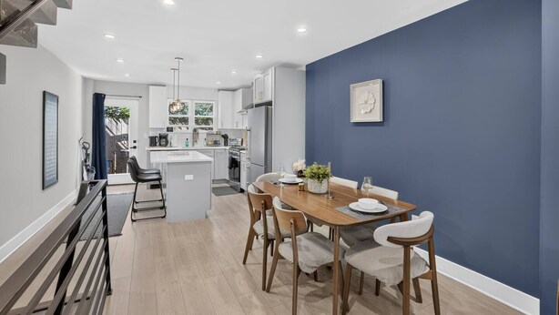Une cuisine moderne avec des meubles blancs, un îlot central et un coin repas comprenant une table et des chaises en bois.