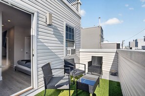 A modern outdoor patio with a sofa, two chairs, and a table, surrounded by a low white wall and a grassy area.
