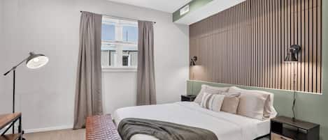 A modern bedroom with a bed, bedside tables, a desk, a bench, and a window with curtains.