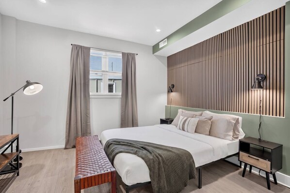 A modern bedroom with a bed, bedside tables, a desk, a bench, and a window with curtains.