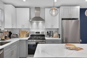A modern kitchen with white cabinets, stainless steel appliances, and a marble countertop.