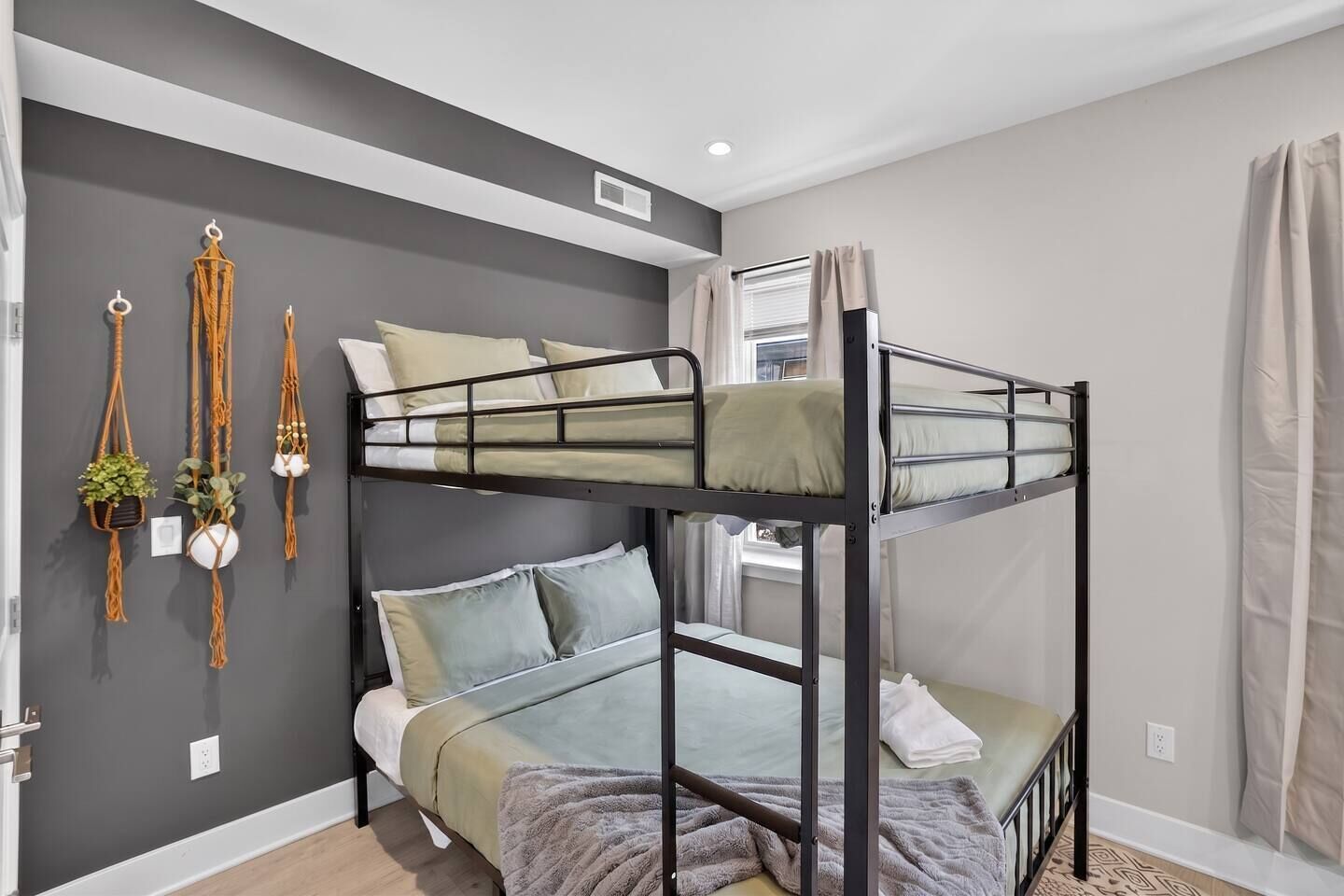 A bunk bed room with grey walls, a window with curtains, and macrame wall hangings.