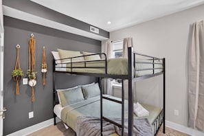 A bunk bed room with grey walls, a window with curtains, and macrame wall hangings.