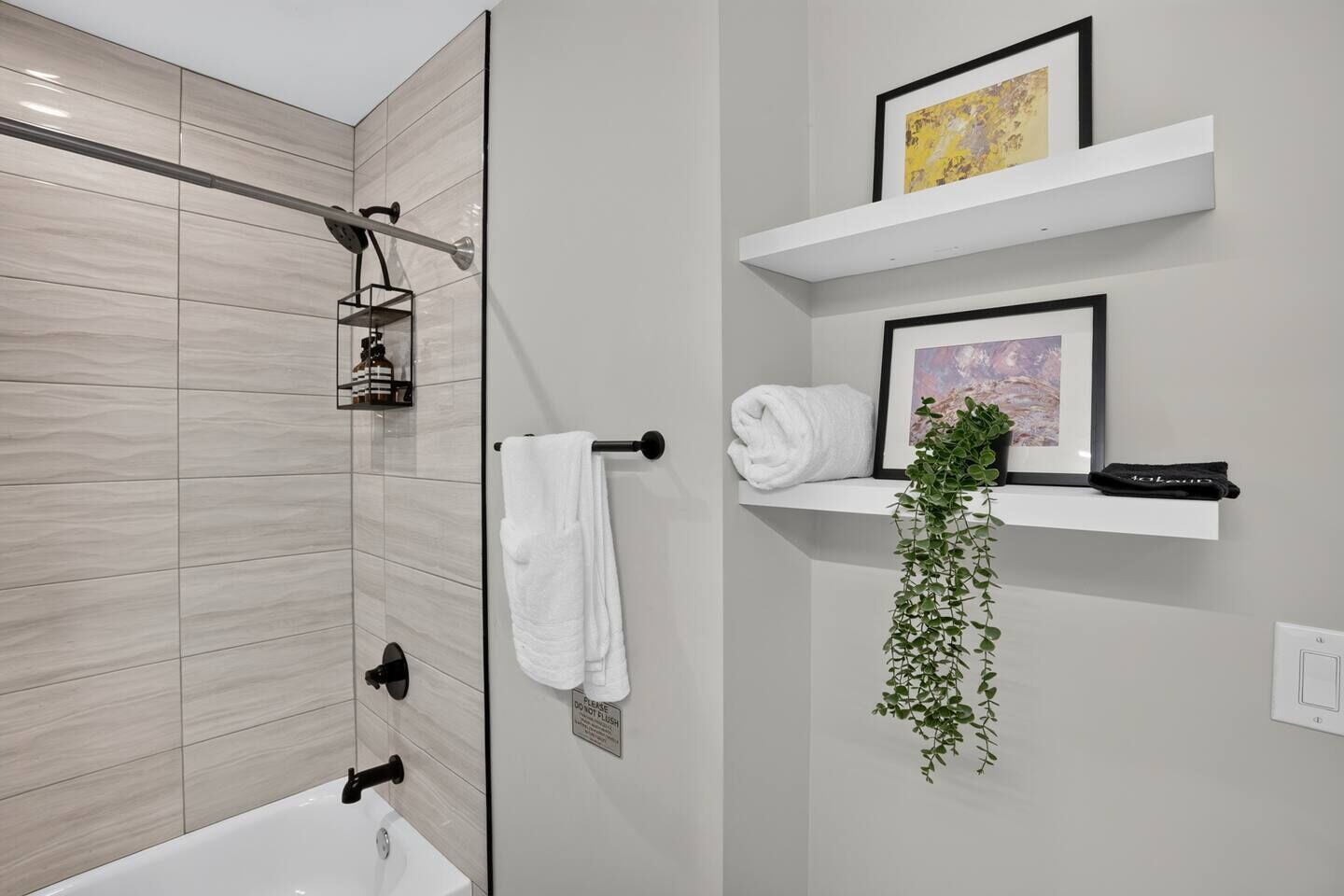 A modern bathroom with a shower, a toilet, and a sink. There are white towels and a plant on a shelf.