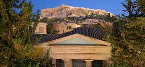 A building with a sign reading 'ΔΗΜΟΤΙΚΗ ΕΞΩΩΑ' and a view of a hilltop structure in the background. - Wonderful apartment in Plaka (Athens)