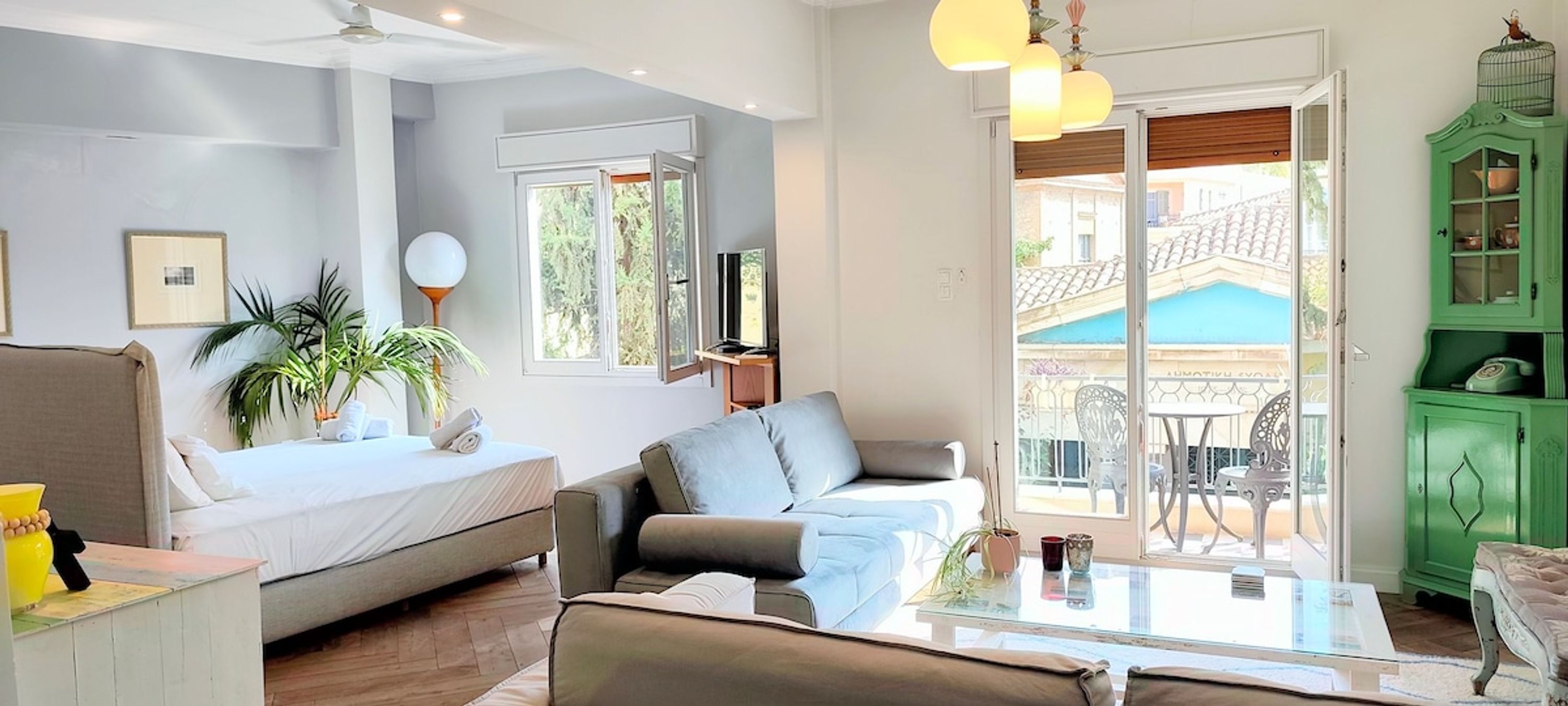 A modern living room with a sofa, a coffee table, and a TV. There is a balcony with a view of the outside.