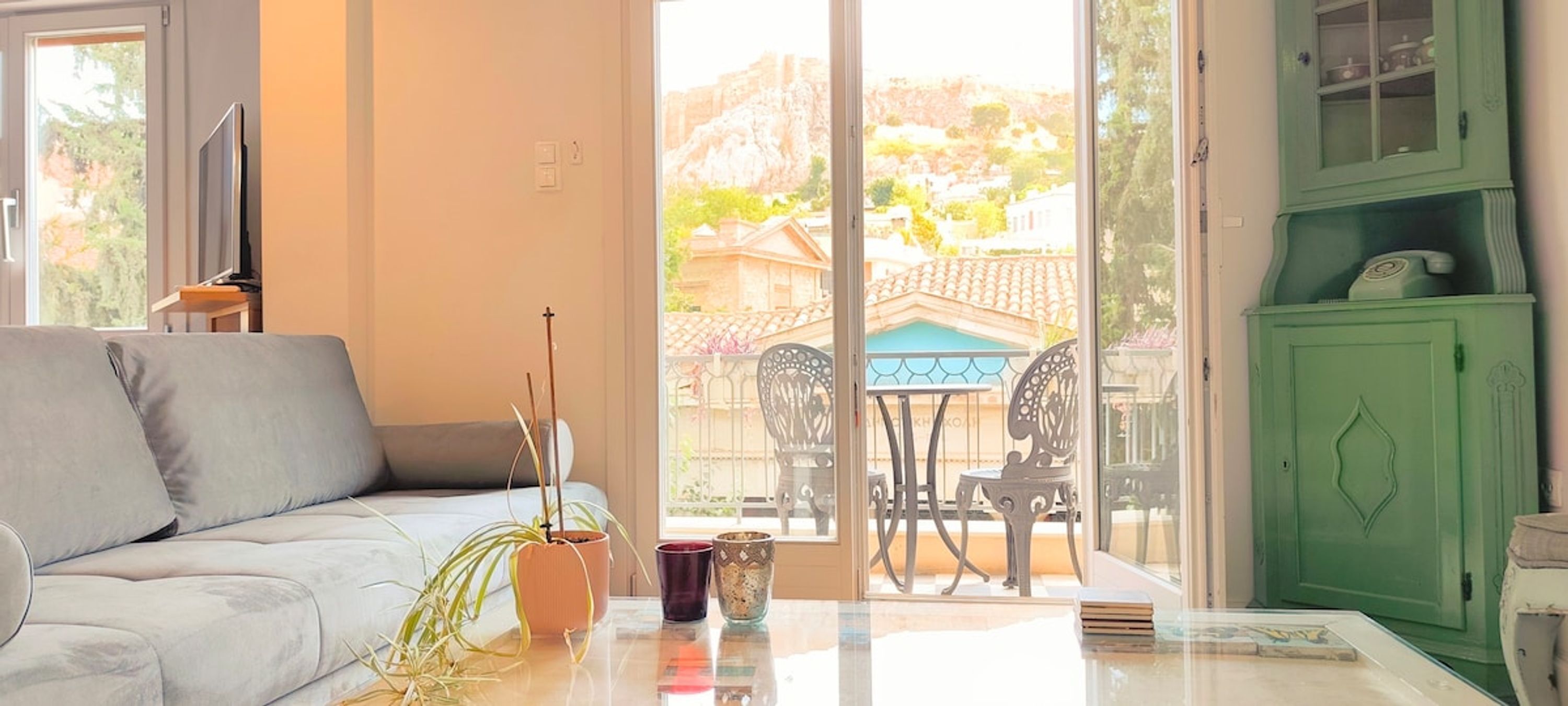 En stue med en sofa, et bord med en plante og en kop, et grønt skab, samt udsigt til en balkon med havemøbler.
