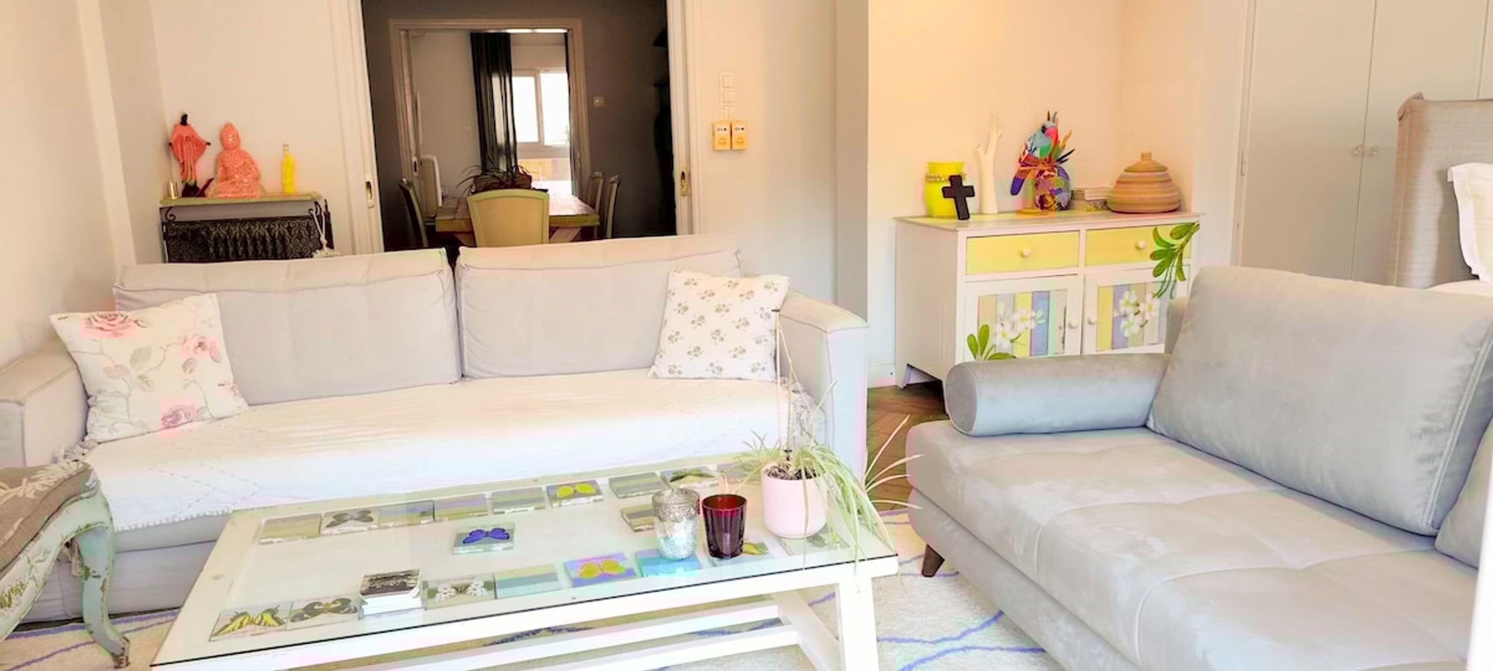 Una sala de estar con un sofá blanco, una mesa de centro de vidrio y un aparador con adornos.