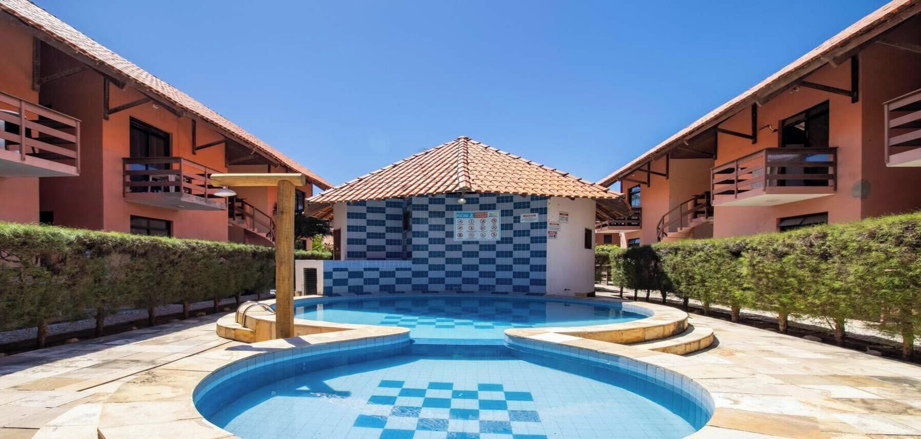 A pool area with a checkered pattern, surrounded by buildings with balconies and a tiled roof.