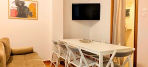 Ein Wohnzimmer mit einer Couch, einem Esstisch mit Stühlen, einem an der Wand befestigten Flachbildfernseher und einer Tür mit Vorhang.