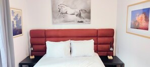 Ein Schlafzimmer mit einem roten, bezogenen Kopfteil, einer weißen Bettdecke, zwei weißen Kissen und zwei Nachttischen mit Lampen.